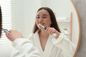 Woman brushing her teeth in front of bathroom mirror