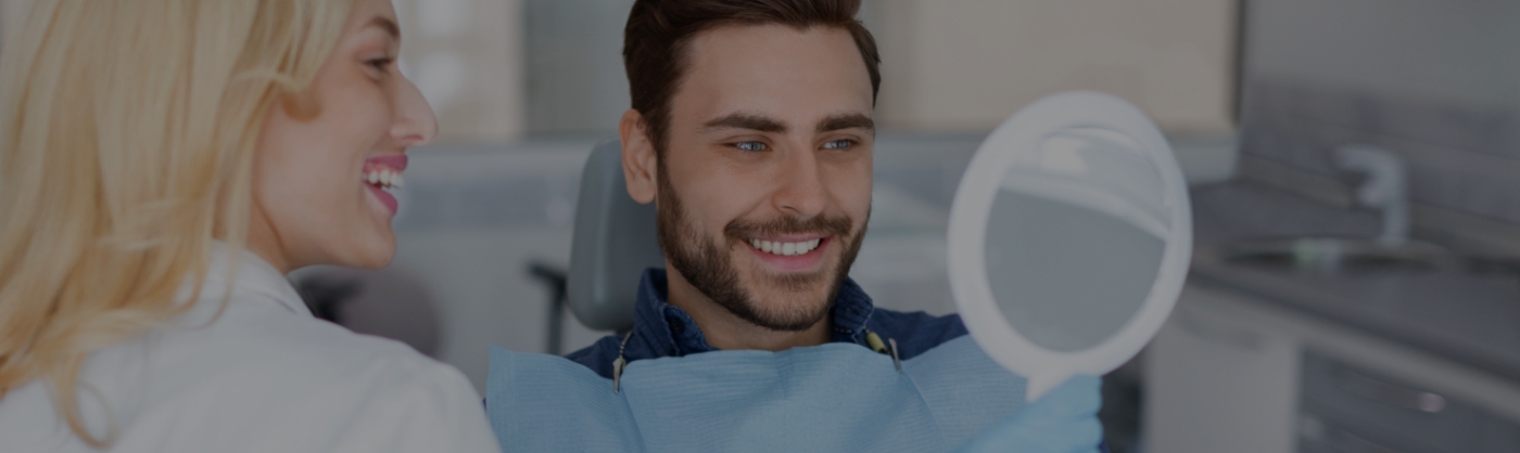 man smiling in hand mirror at a dental office in Encino