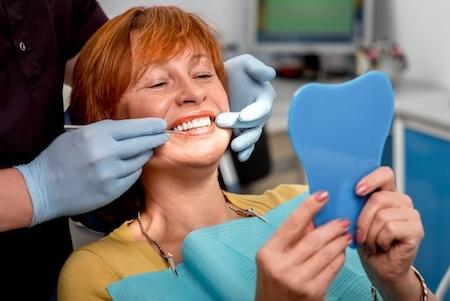 Older woman looking at teeth with handheld mirror, encino ca